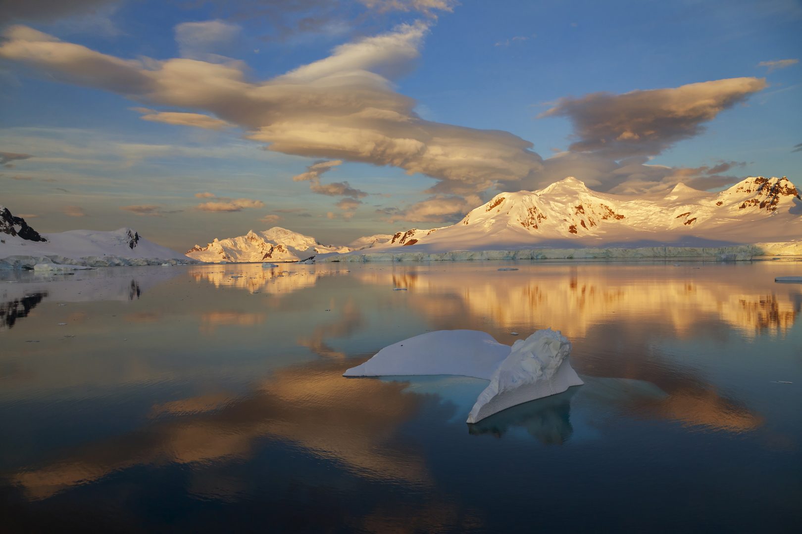 Gold lit mountain range under a lenticular cloud, mirrored in still water.